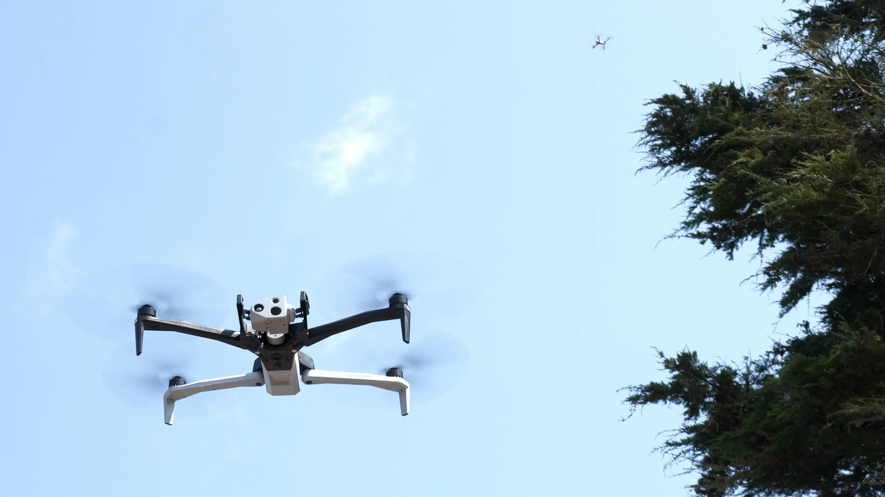 Two inspection drones flying utility powerline route against open sky